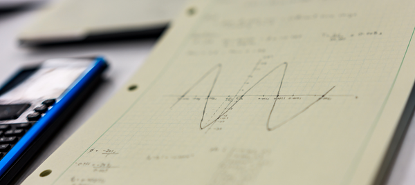 A calculator and a sheet of engineering paper with hand drawn graphs on a table.